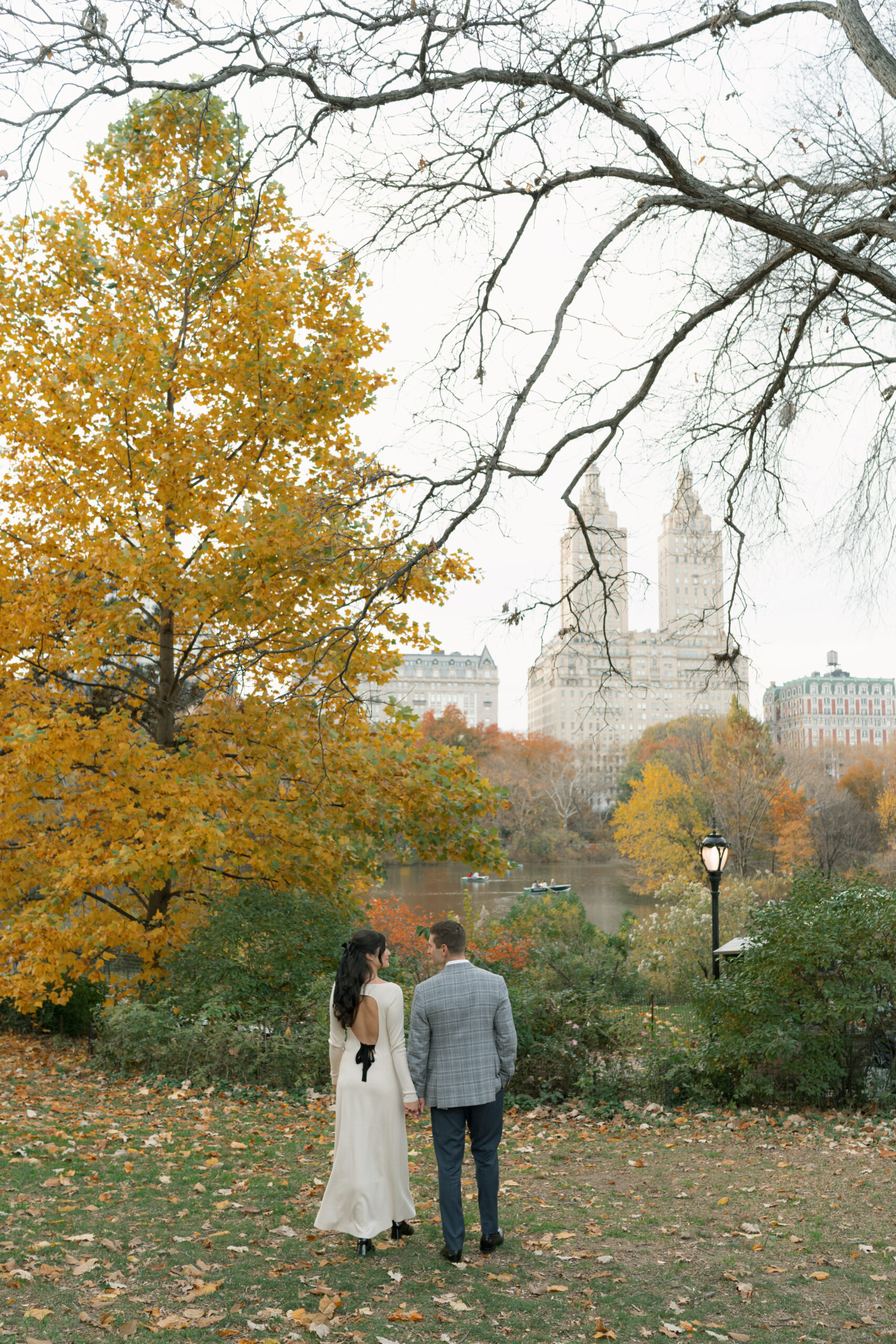 Engaged couple walks in NYC Central park in the fall, with the iconic NYC cityscape in the distance.
