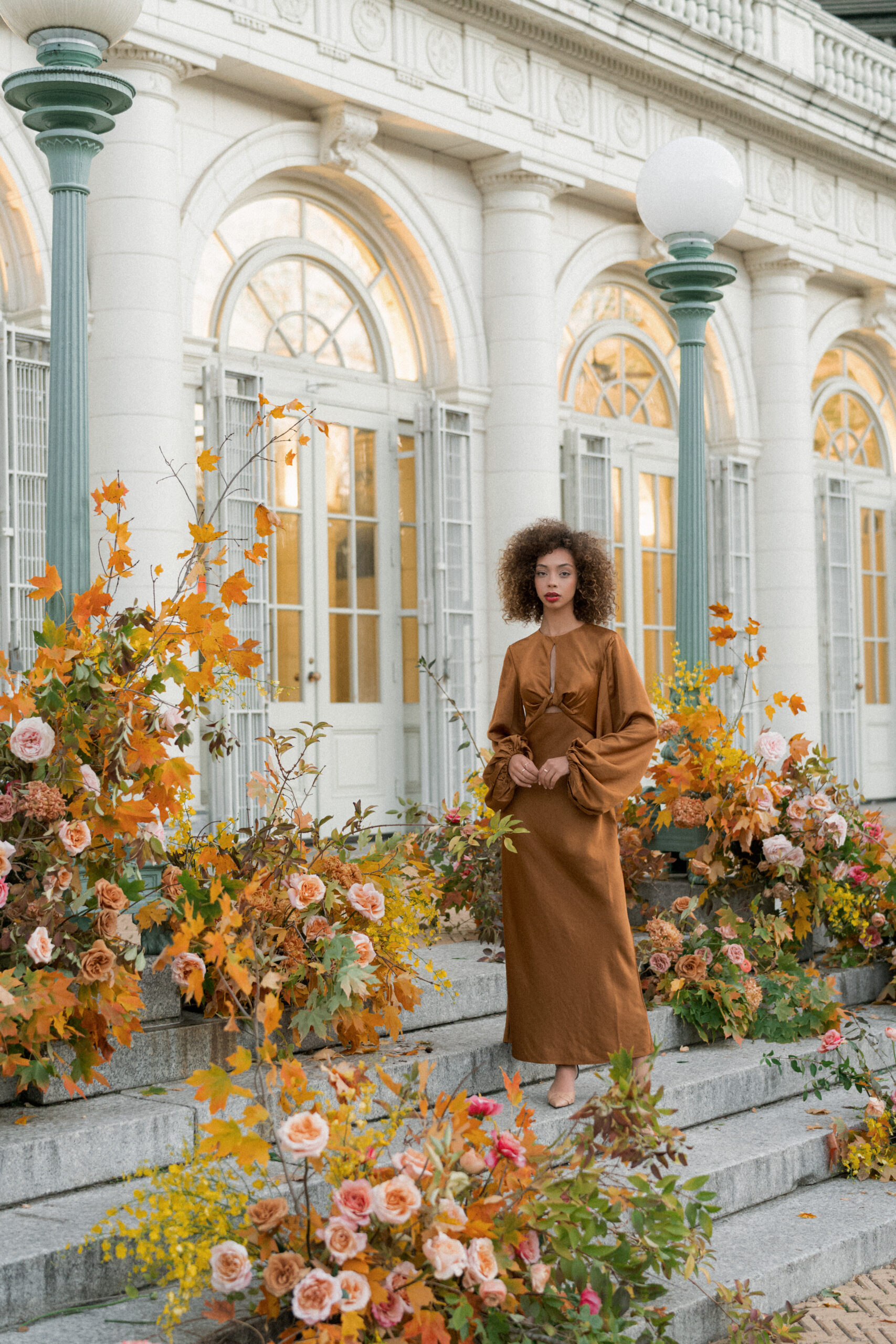 Model stands in golden dress amongst a lush autumn floral installation at the Brooklyn Boathouse in New York.